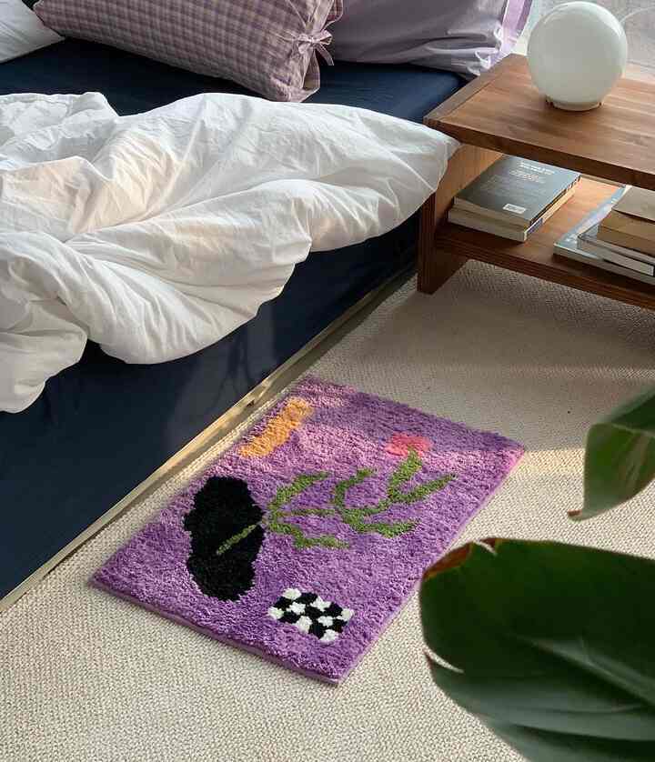 落ち着いたネイビーカラーのベッドと、鮮やかな紫色のラグが配置された寝室、木目調のサイドテーブルと白い寝具が調和した空間