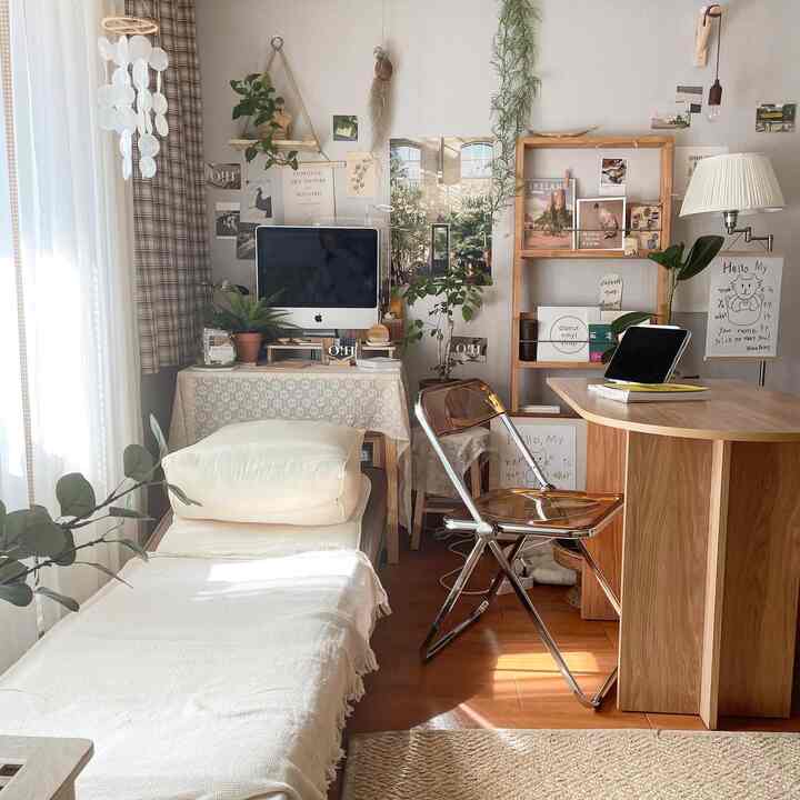 Natural-toned single household home office featuring wooden desk, single bed, and assorted plants creating cozy atmosphere