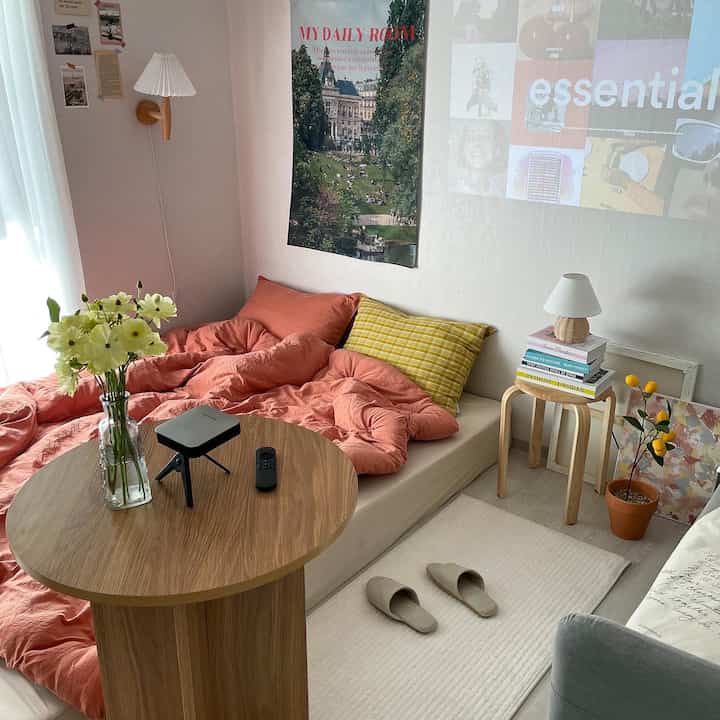 Cozy two-person bedroom with pink bedding and wood tone round table, featuring modern and clean layout