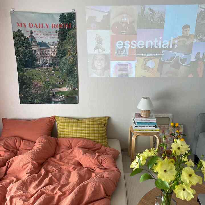 Cozy low-profile bedroom with warm terracotta tones, yellow flowers in a vase, stool beside lamp and books, with projector casting images on wall