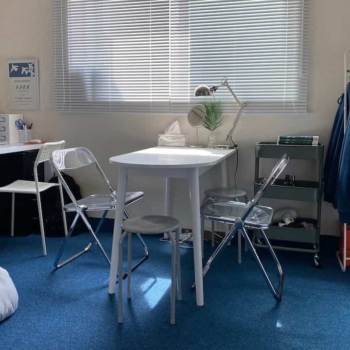 ブルーのカーペットとホワイト家具が配置されたワンルームの一人暮らし、清潔でモダンな雰囲気の空間