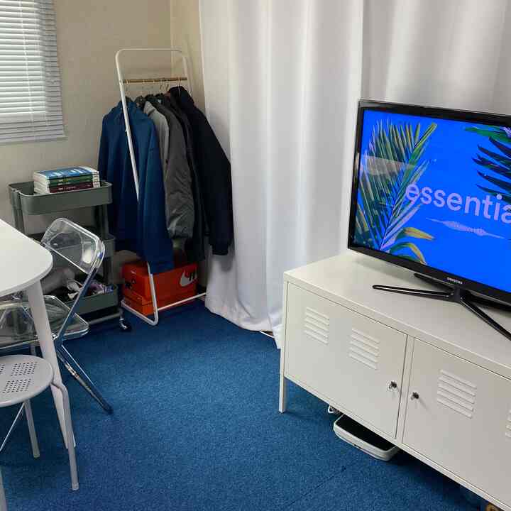 白と青のトーンの狭い部屋、白いキャビネットとカーテン、コートラックとキッチンワゴンが配置されたシンプルなインテリア