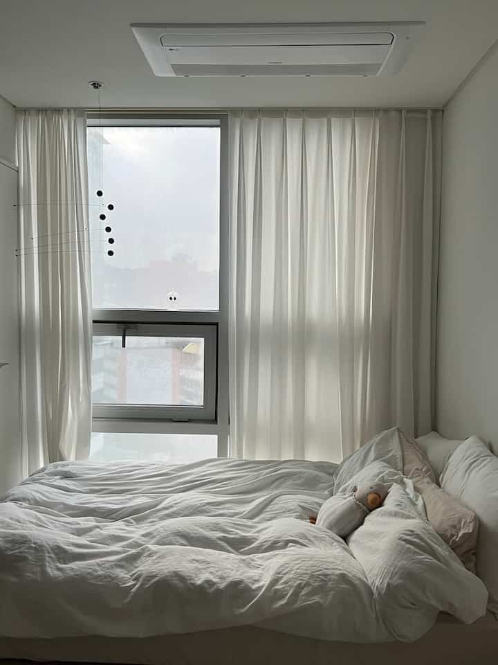 White-toned bedroom featuring a large window and white bedding, showcasing a simple and cozy atmosphere