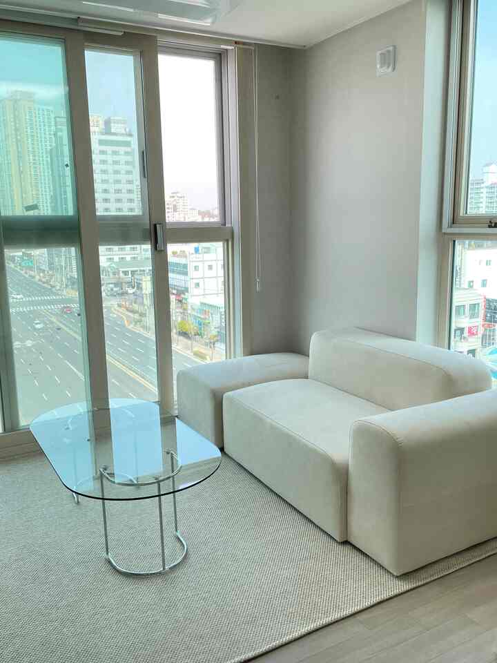 白を基調としたリビングに、2人掛けのソファと透明な強化ガラスのコーヒーテーブル、ナチュラルカラーのサイザルラグが配置されたモダンなインテリア