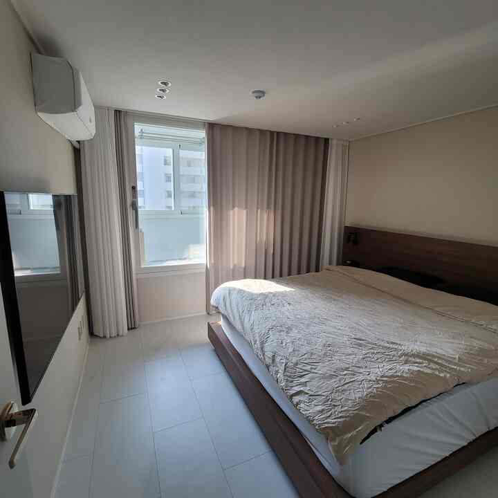 Modern bedroom in beige and white tones featuring a large bed and beige curtains in a clean, minimalistic space