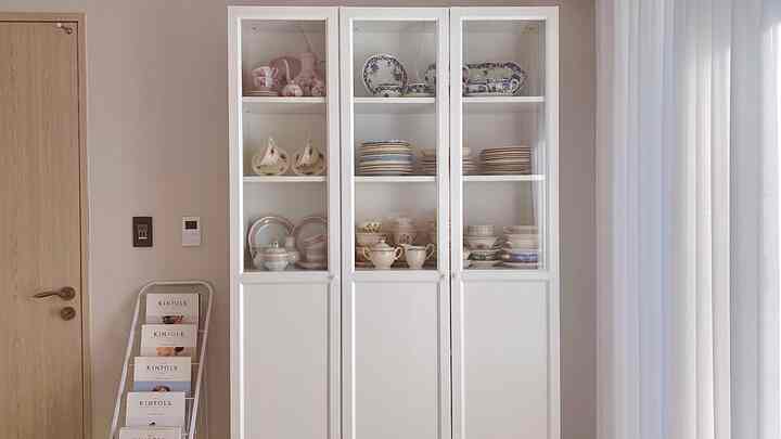 White-toned living room or kitchen space featuring a white cabinet displaying vintage tableware in a calm atmosphere