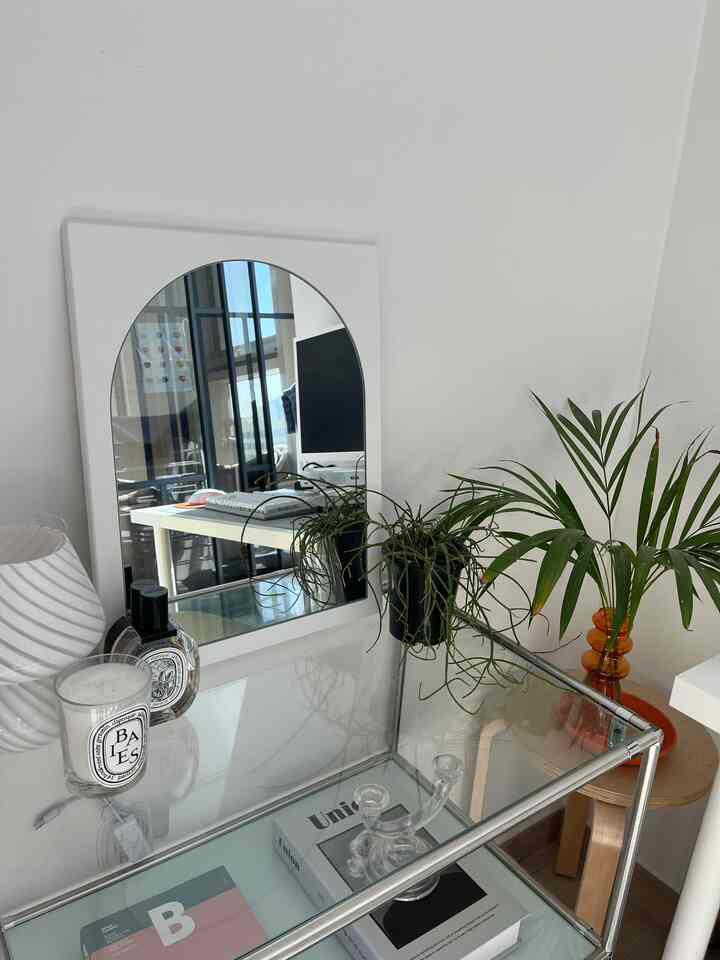 白い壁と鏡があるナチュラルモダンなデスク空間、植物とキャンドルが配置された整ったインテリア