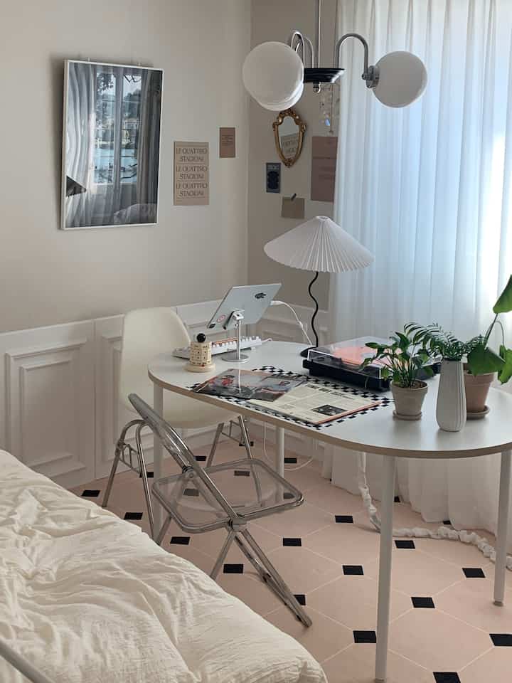 Bright and clean home office and bedroom with dominant white and wood tones, featuring a transparent chair and round table
