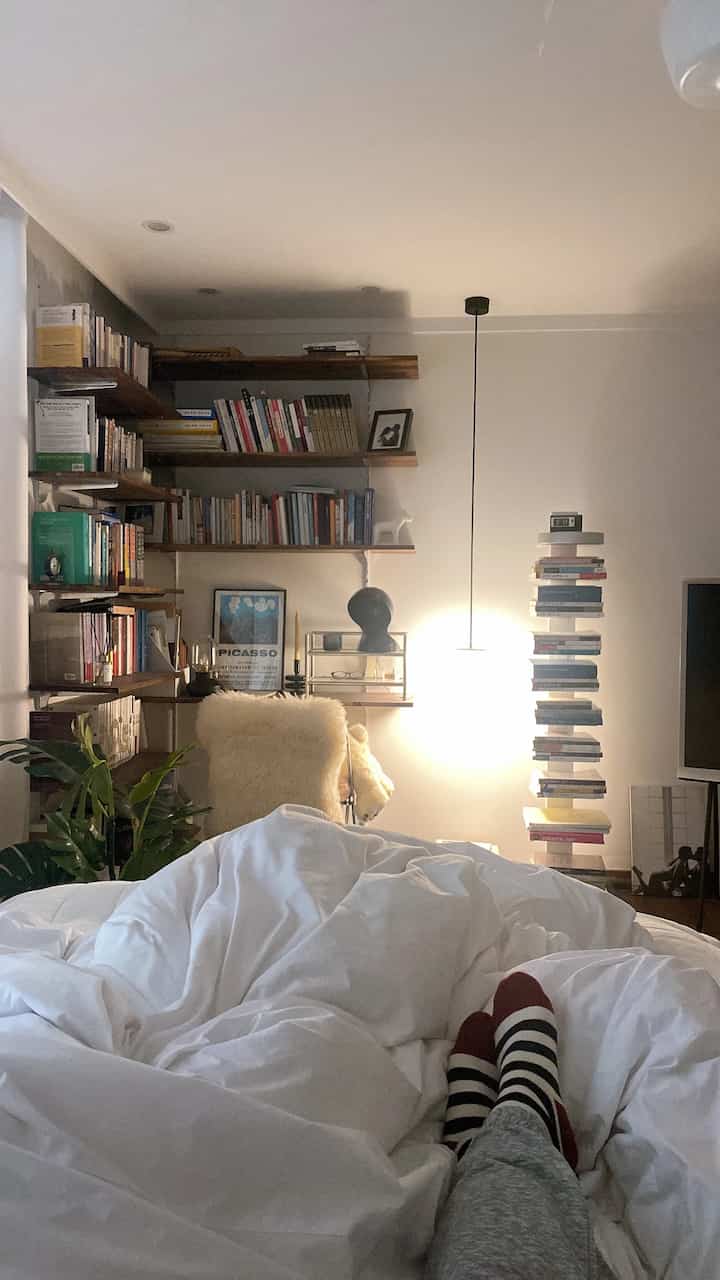 Cozy bedroom with white bedding, vintage modular shelves, and pendant lighting creating a warm atmosphere