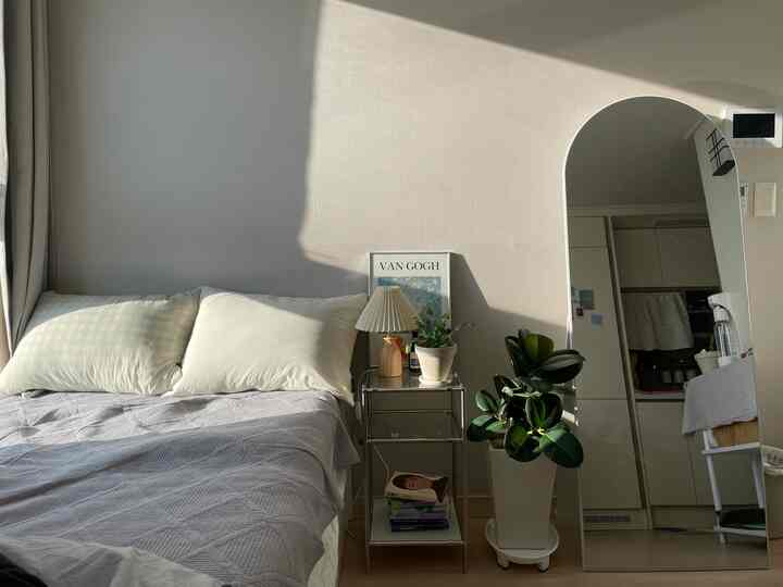 自然なベージュトーンの壁と枕、ナイトテーブル、アーチ型の全身鏡が配置されたシンプルな寝室のインテリア