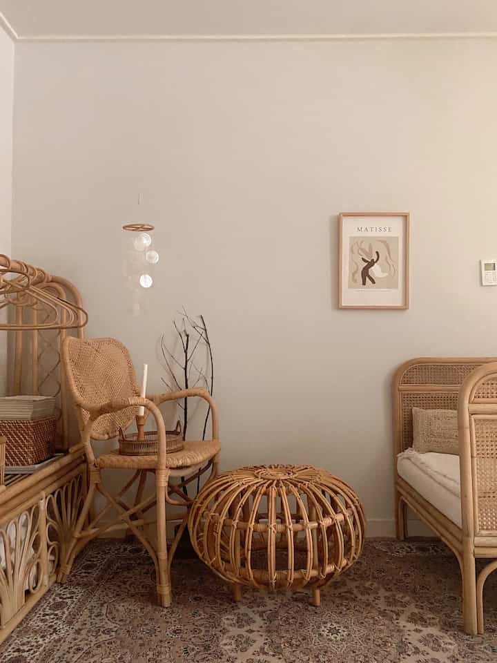 Beige and natural toned living room featuring rattan armchair, stool, and framed art in a simple, warm space