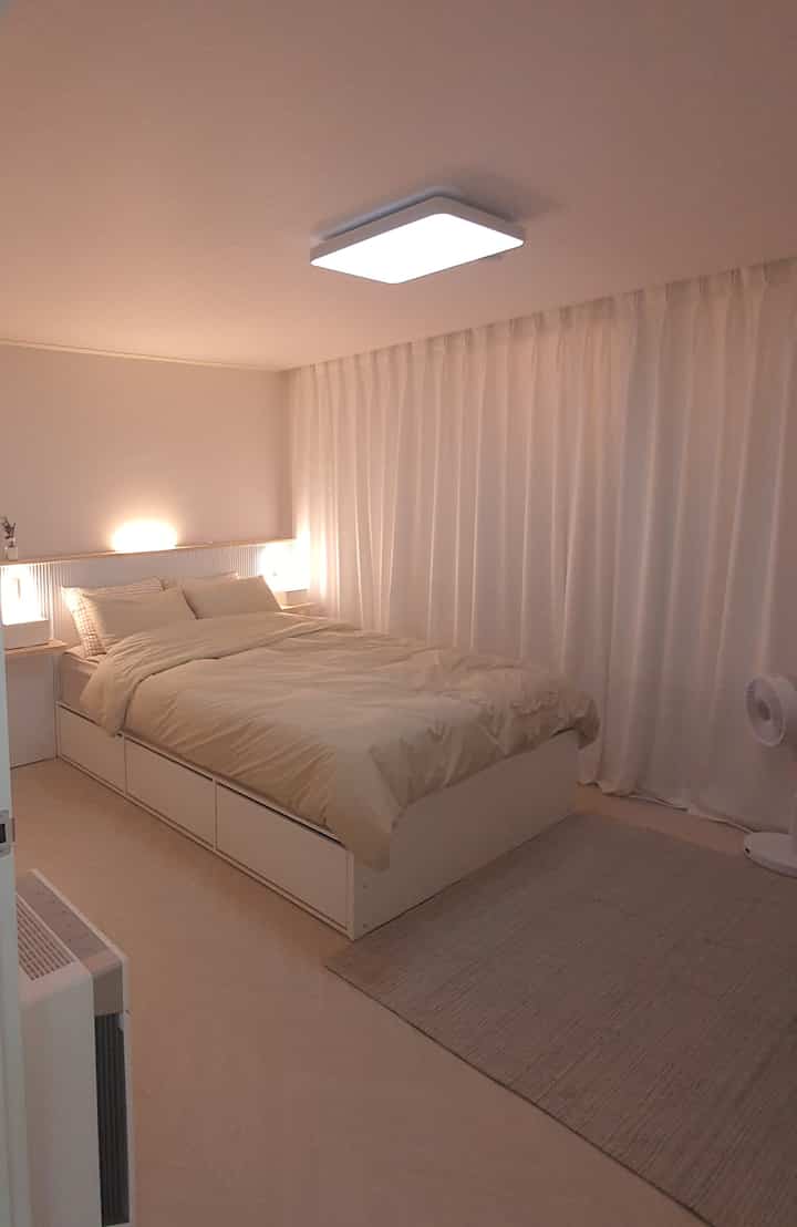 White and beige toned bedroom featuring a storage bed, curtains, and rug with a modern and simple atmosphere