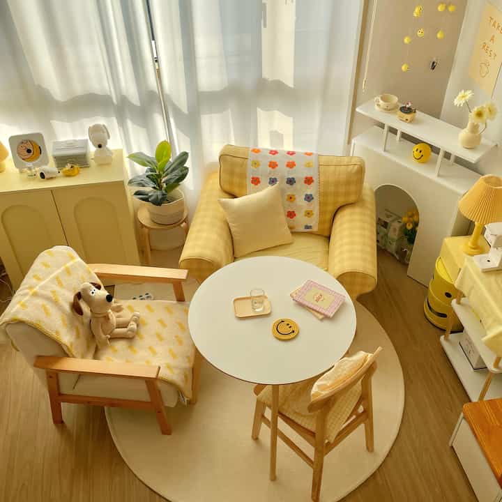 Bright yellow-toned living room featuring yellow armchair, round white table, and wooden chair arranged cozily