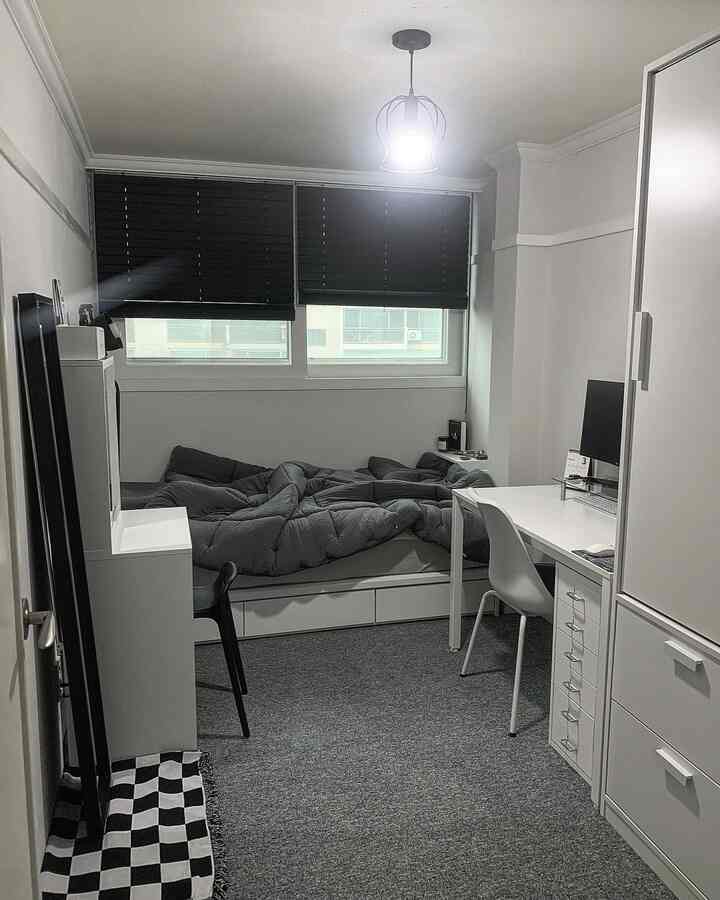 A modern single household bedroom with gray carpet and white furniture, featuring a computer desk for remote work