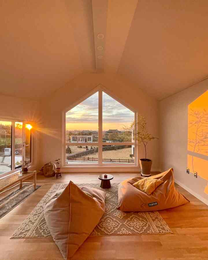 Warm yellow-toned living room featuring large windows, bean bags, and a rug in a cozy natural interior