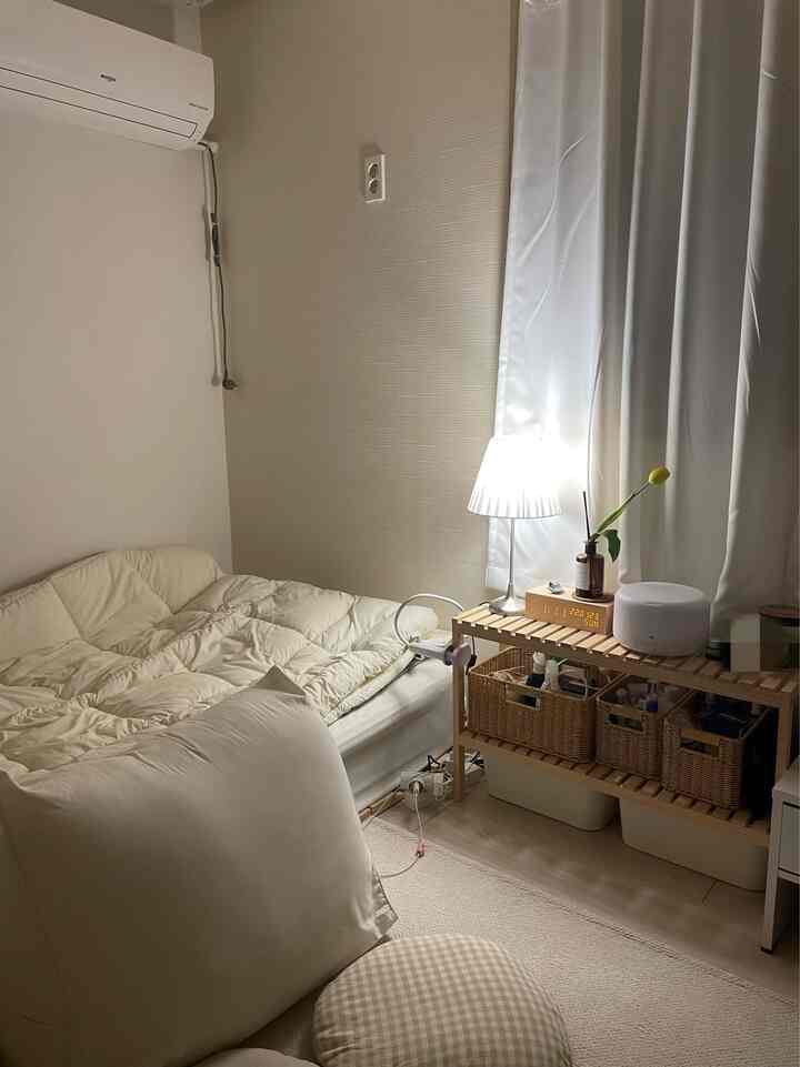 Natural-toned compact small bedroom featuring beige bedding, wooden storage shelf, and soft ambient lighting creating a cozy atmosphere