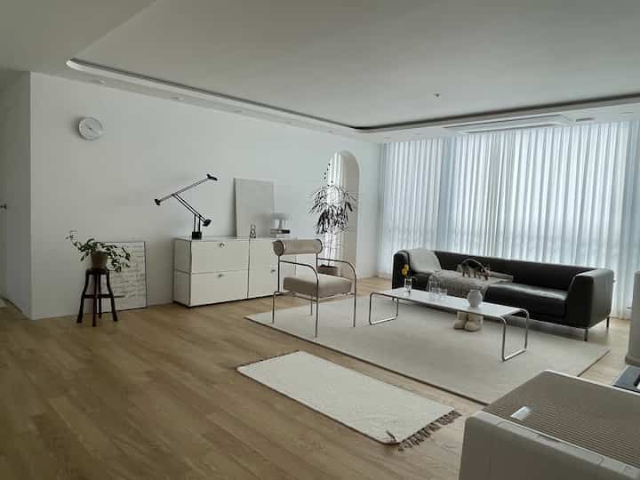 A white and natural toned living room featuring a black sofa and ivory armchair in a modern setting