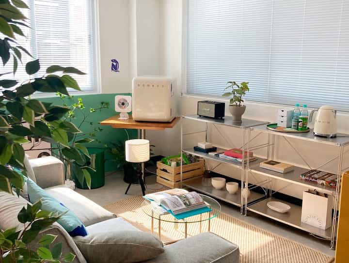 Bright white and green toned living room home office featuring mid-century modern furniture and plants creating a cozy healing zone