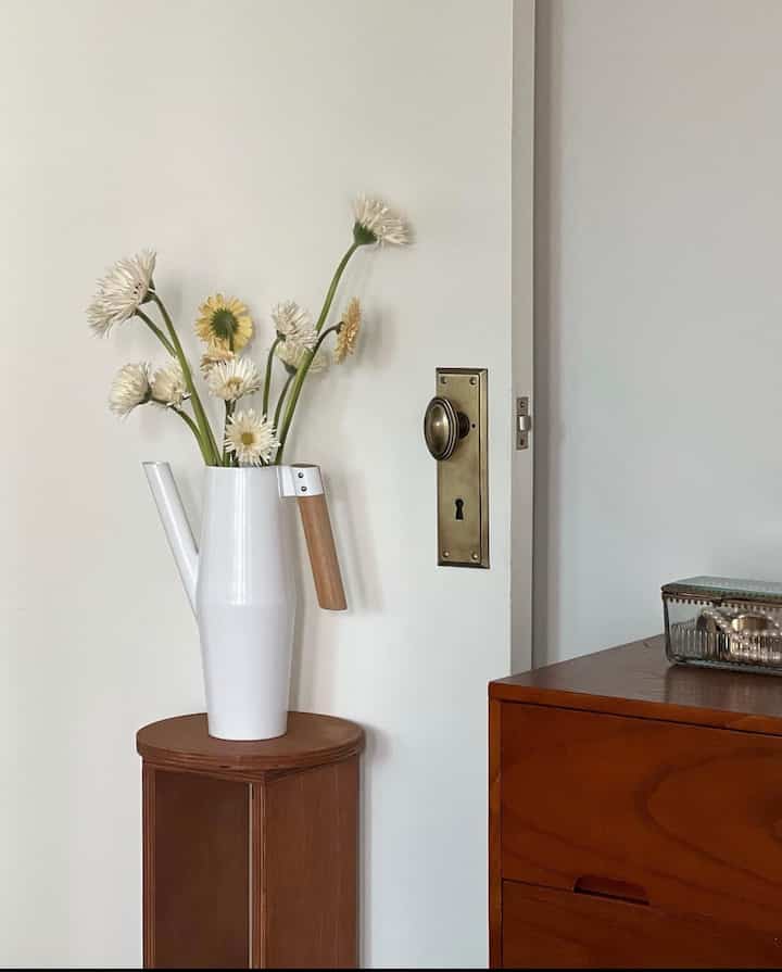 Mid-Century Modern space with white wall background and brown wooden chest, featuring a white vase on stool as natural decor accent