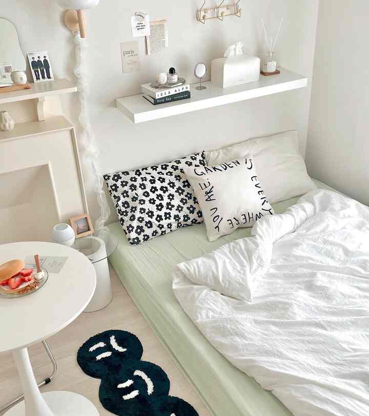 Natural color and white toned studio bedroom featuring black patterned cushions and delicate accessories, creating a modern and clean space