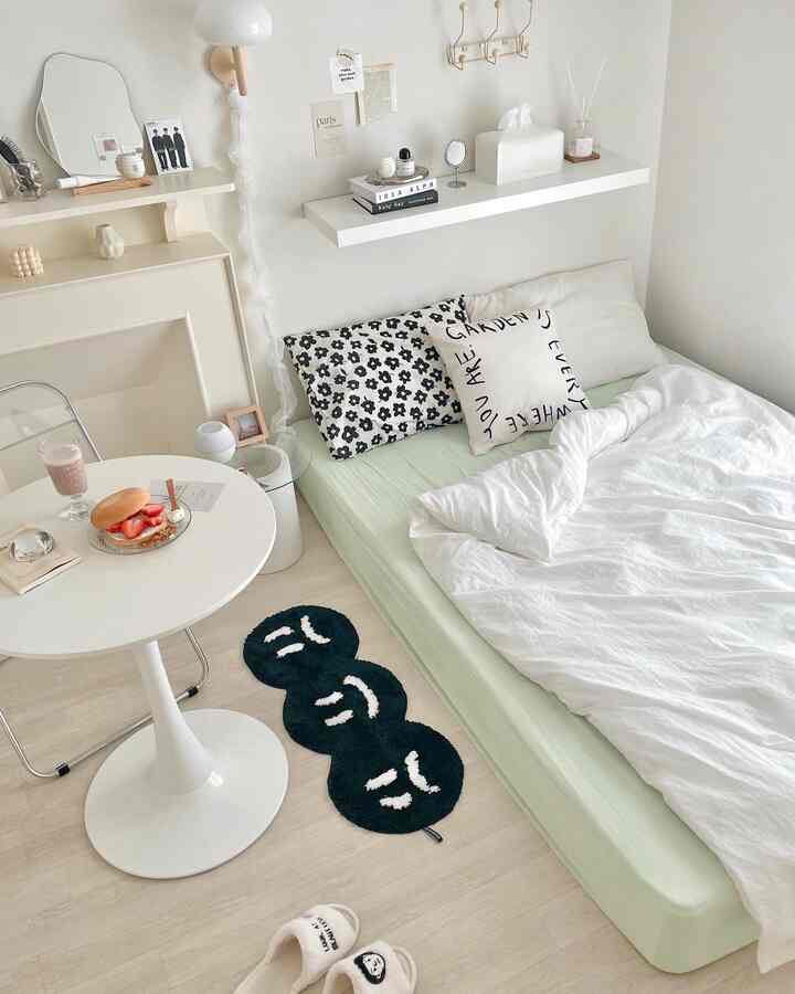 Mint and white toned single household bedroom featuring a round table and wall shelf in a simple, cozy setting