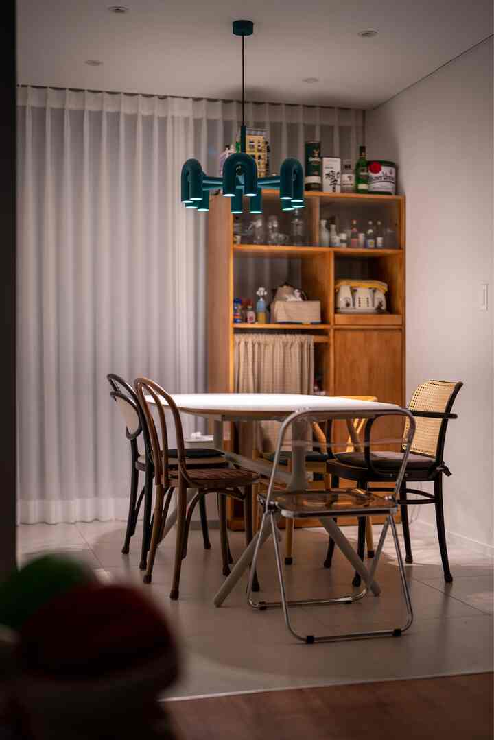 Cozy dining room with warm wood tones and white color, featuring diverse chairs and a blue chandelier with inviting atmosphere