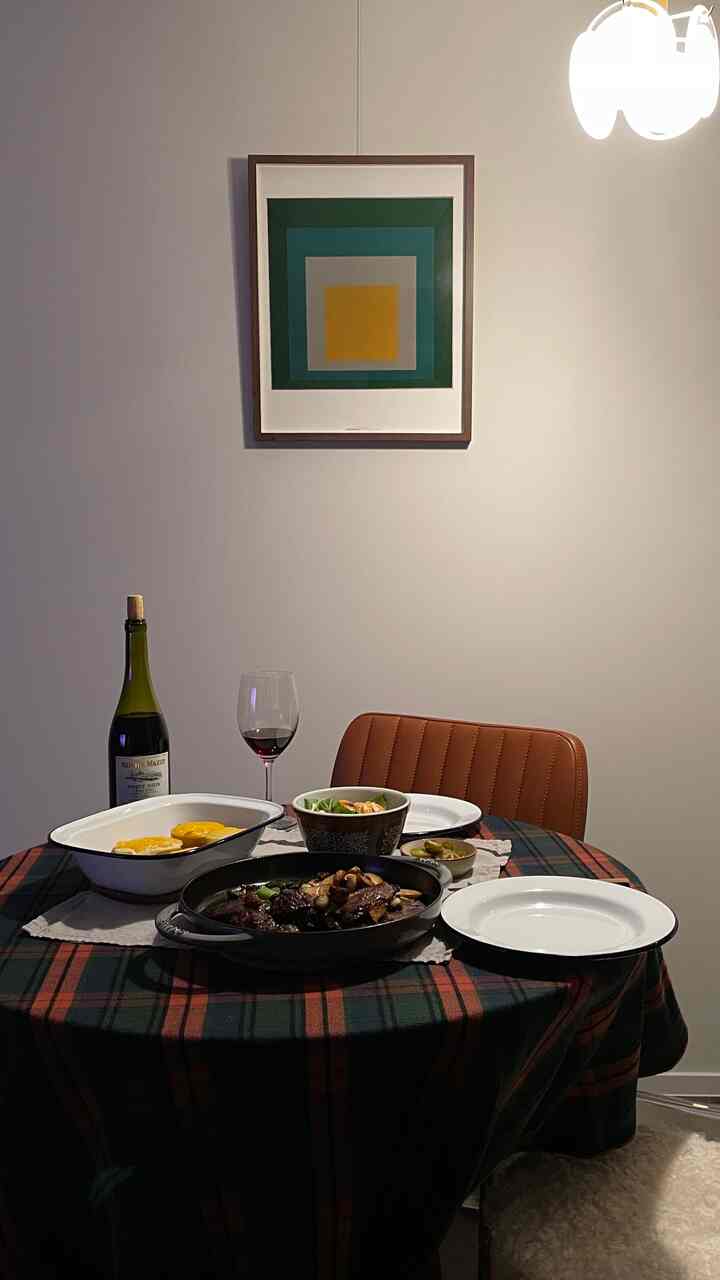 Green and brown toned dining room featuring a round table with brown chairs, framed wall art, and wine with food set for a cozy atmosphere