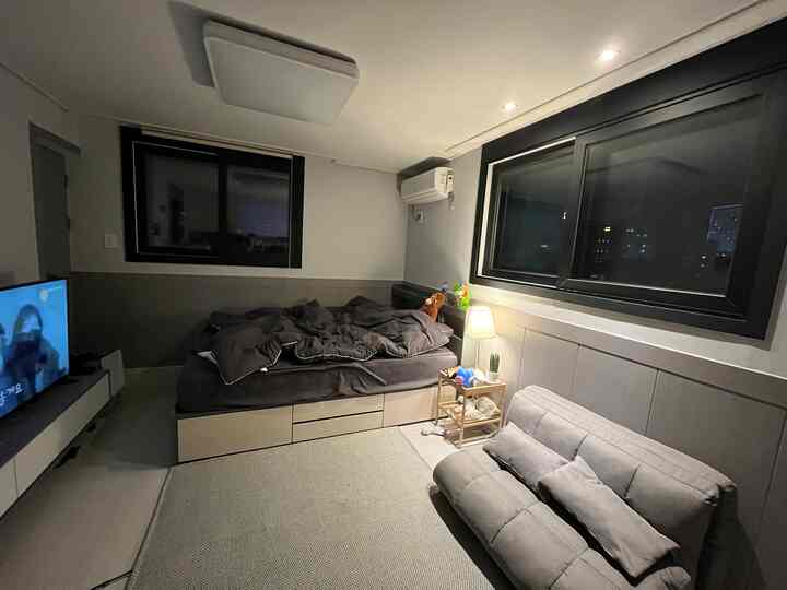 グレーとホワイトのトーンのワンルーム、収納ベッドとファブリックソファが配置された居心地のよい一人暮らしの空間