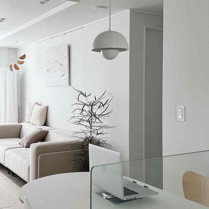 White and beige toned living room and kitchen featuring beige sofa and round dining table with a laptop, simple and natural interior