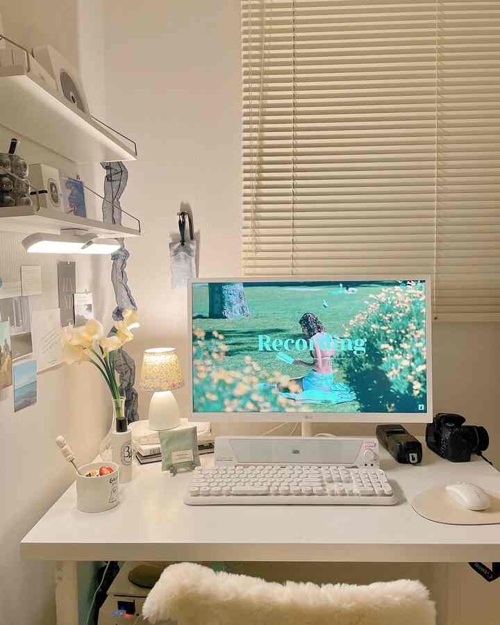 White-toned compact desk space featuring monitor, keyboard, and mood lamp with a clean and cozy home office atmosphere