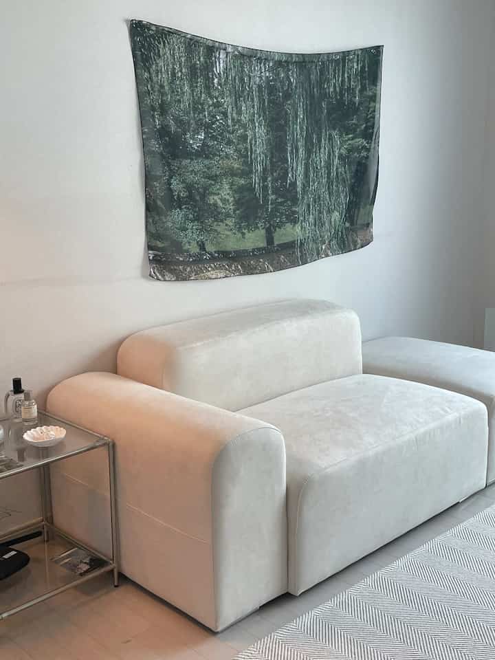 白とグレーのトーンのリビングルーム、ミッドセンチュリーモダンスタイルの広いソファとガラスのサイドテーブルが配置された清潔感のある空間