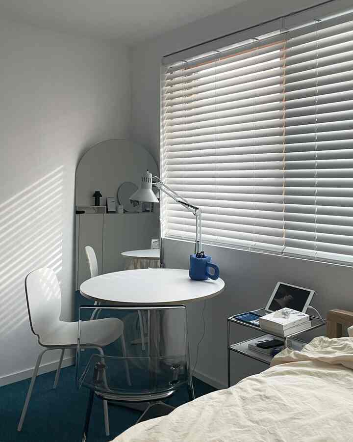 Small bedroom space in white and blue tones featuring a round table and multifunctional furniture in a modern, clean design