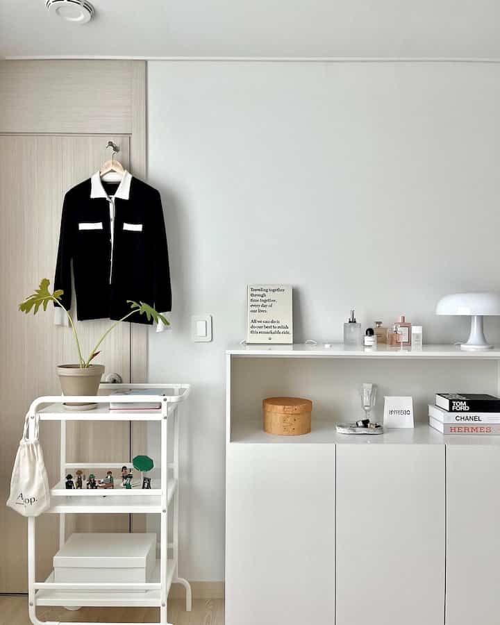 ホワイトとナチュラルカラーのウォークインクローゼット、シンプルなキャビネットとトロリー、洗練された照明と小物が調和したミニマルなインテリア