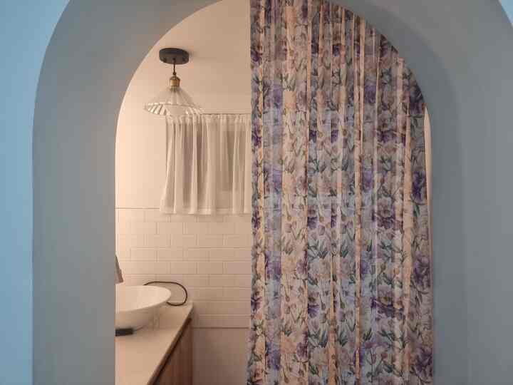 A powder room interior with an arched entrance, featuring white tones and floral curtains harmoniously arranged