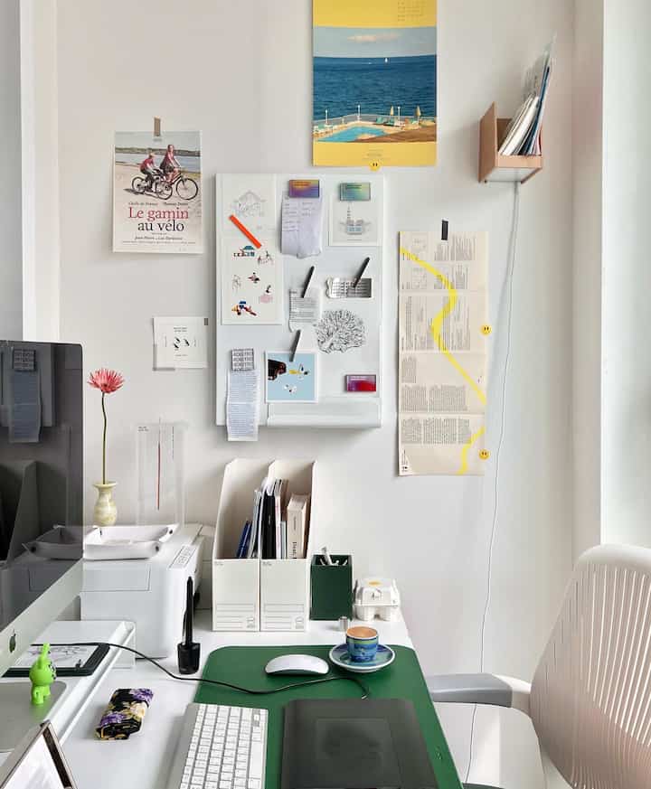 White and green toned home office space featuring an organized desk with decor items and postcards with posters pinned on the wall, conveying a neat atmosphere