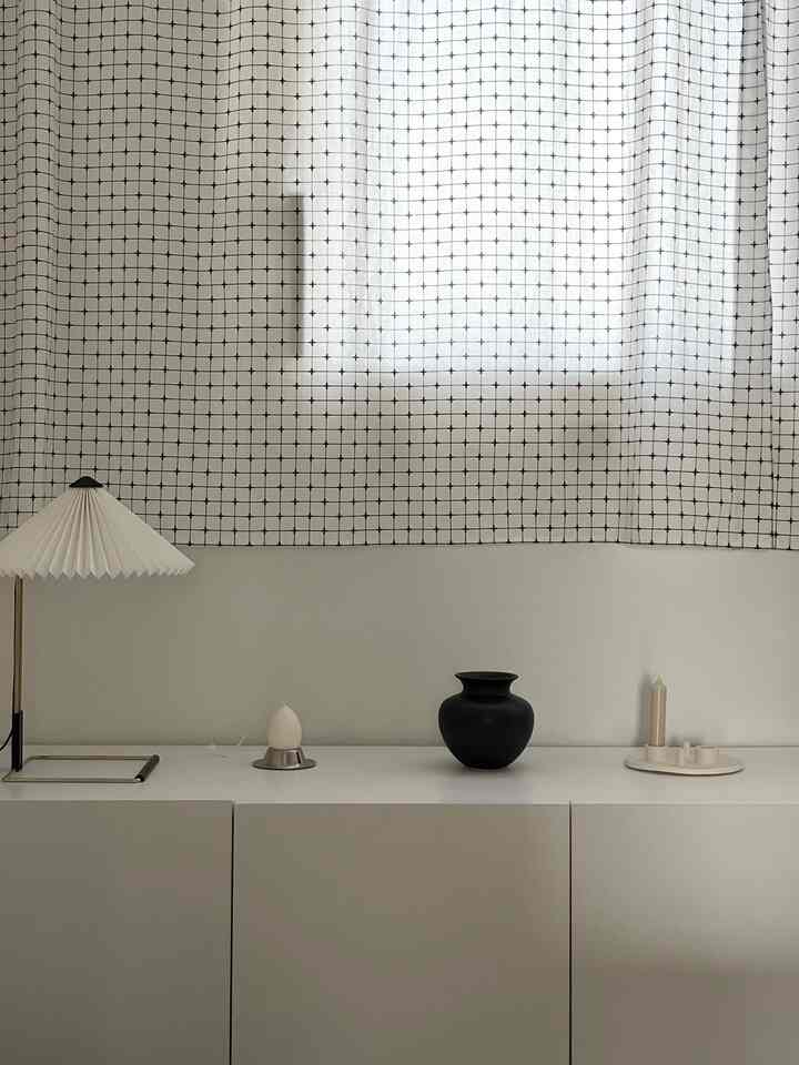 A beige and white toned study featuring minimal table lamp, black vase, and candles arranged neatly