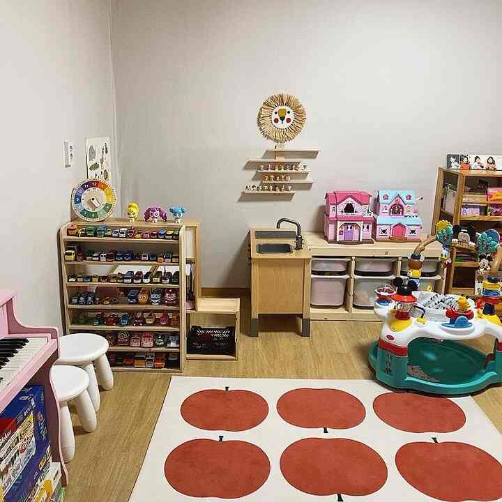 Natural wood tones and white with red accents in a cozy kids' room, featuring various toys and play furniture arranged neatly