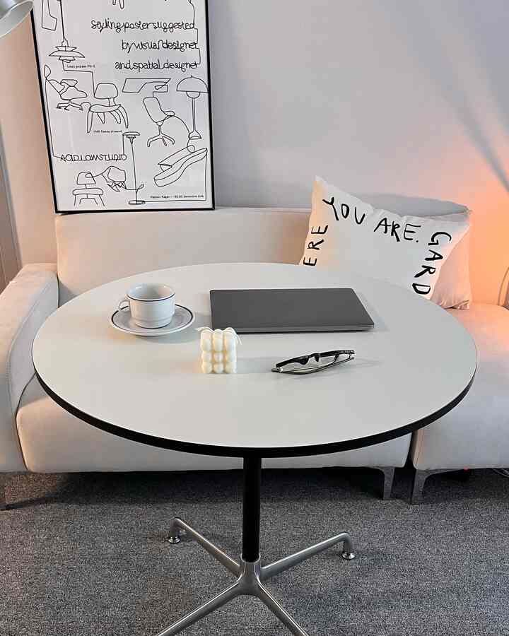 A white-toned living room featuring a Mid-Century Modern sofa and round table in a clean, minimalistic space