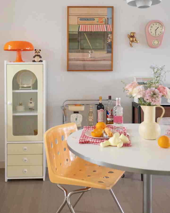 オレンジとベージュの色調が調和するヴィンテージ風ダイニング、丸いダイニングテーブルとヴィンテージキャビネット、壁掛け時計と額縁が印象的な空間を作り出している。