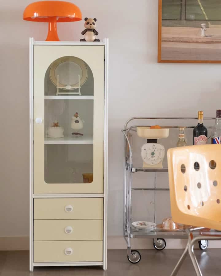 A white and beige toned dining room featuring a vintage cabinet and chrome kitchen cart, creating a warm atmosphere