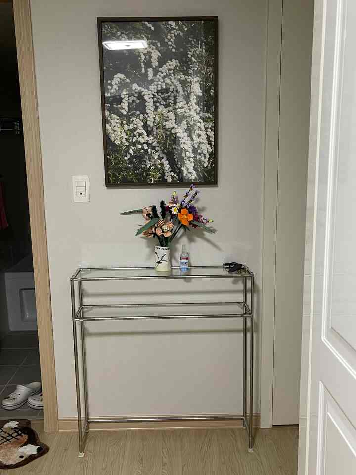 ナチュラルカラーの玄関、木目調の床にステンレス製コンソールテーブルがあり、花瓶と額縁が配置された雰囲気のあるインテリア