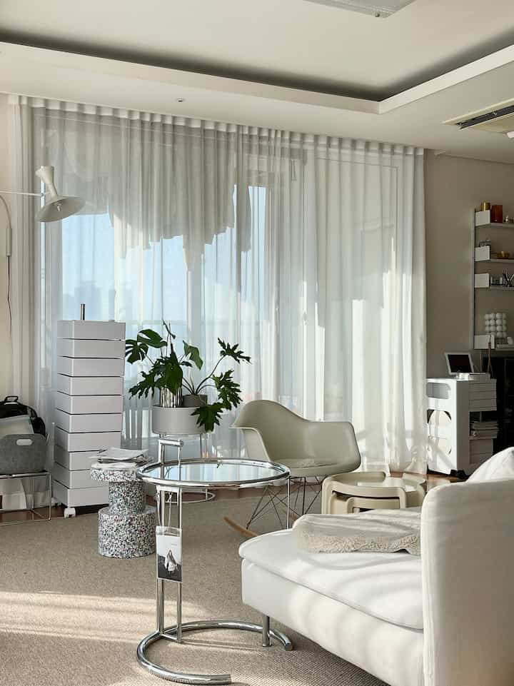 Natural tone living room in white and beige, featuring white armchair, sofa, glass side table, and green plant