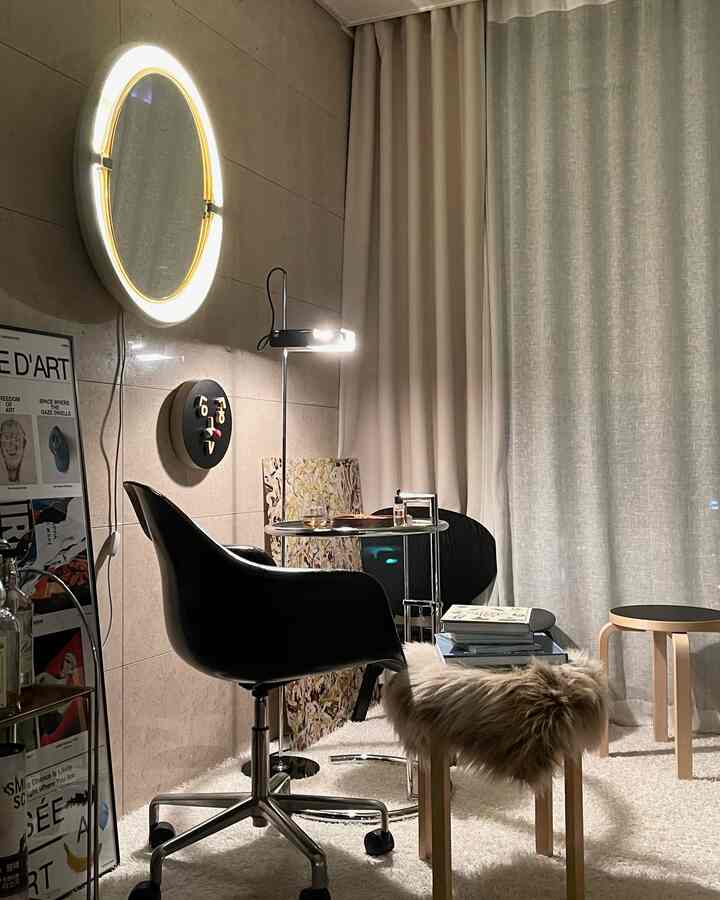 Beige-toned walls and curtains form the backdrop of a modern home office space featuring a black swivel chair, round side tables, and a furry stool creating a cozy atmosphere
