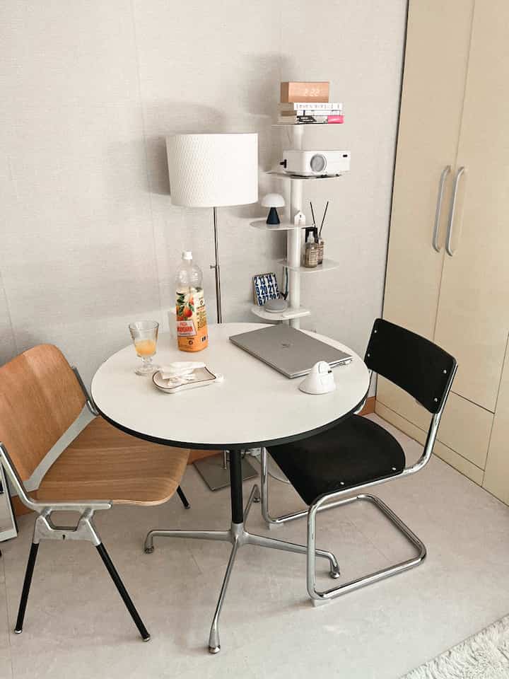 White-toned small kitchen space featuring round dining table, mixed chairs, and a floor lamp creating a cozy atmosphere