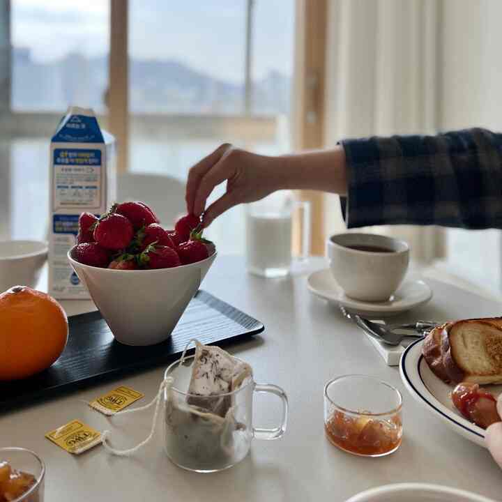 Bright white-toned dining room featuring a bowl of strawberries, toast on a plate, and tea with milk creating a cozy home cafe setting