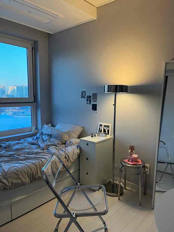 ホワイトトーンの寝室、透明な椅子とメタリックなフロアランプが配置されたモダンで清潔感のあるインテリア