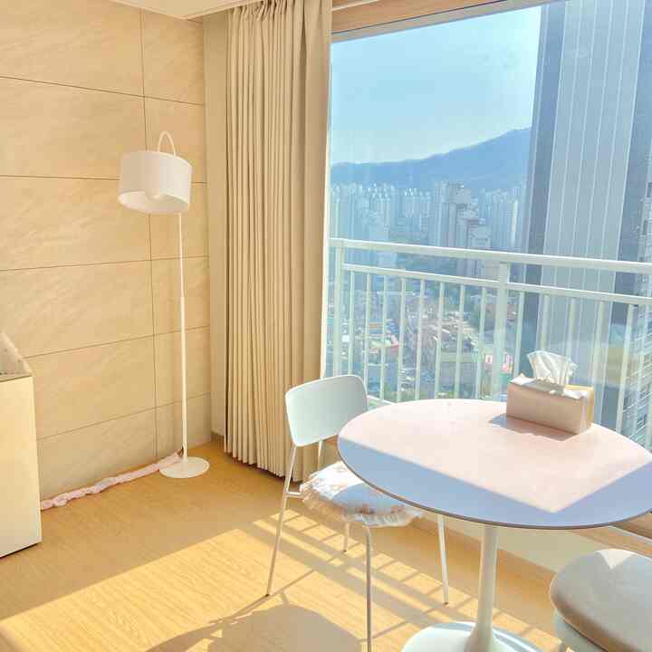 明るくナチュラルな色調のリビングにベージュの遮光カーテンとラウンドテーブル、椅子、フロアランプが配置された印象的なインテリア