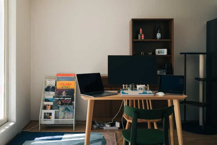 木目調と自然なグリーンの椅子が調和するリビングルームで、ホームオフィスのデスクにモニターと猫用キャットタワーが配置された雰囲気のあるインテリア