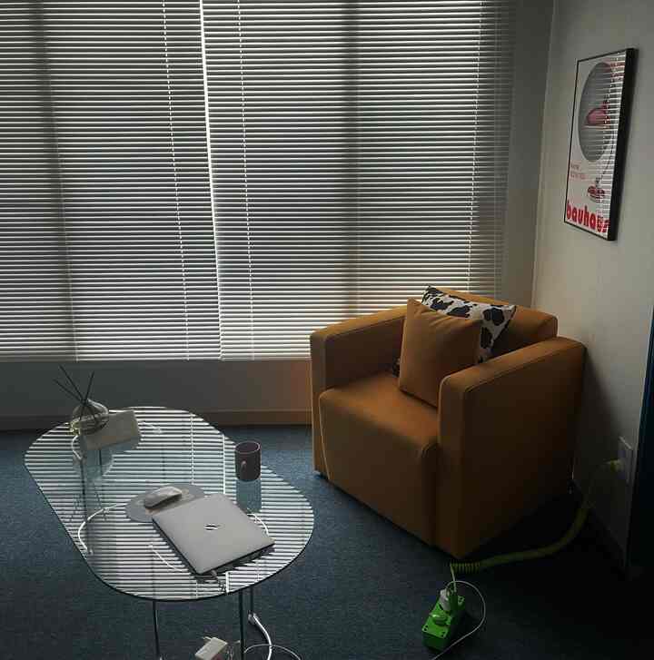 Mid-century modern living room featuring an orange armchair, glass coffee table, and white aluminum blinds with calm atmosphere