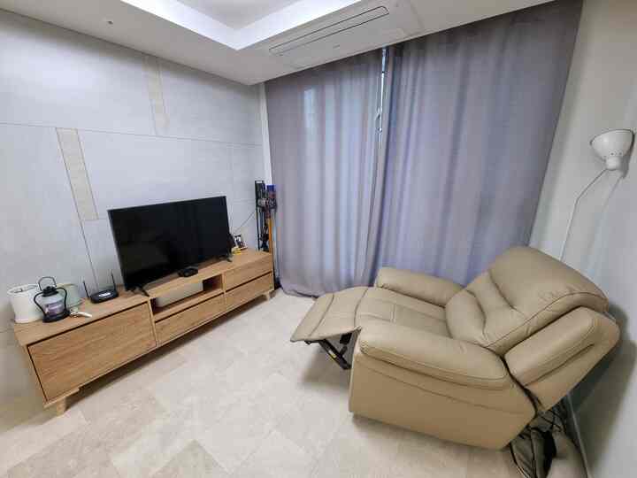 ベージュのリクライニングチェア、ナチュラルウッドのテレビ台、グレーの遮光カーテンが配置されたモダンなリビングのインテリア